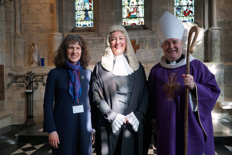 2 women standing next to bishop in purple robes and mitre in a church building