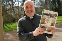 Archbishop standing outside holding an A4 sized book with 5 pictures on the front
