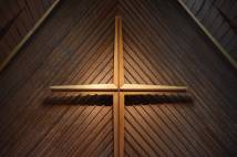 Wooden cross hanging on a wooden backdrop illuminated by light
