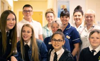 4 school pupils standing with health care professionals behind them, in a care facility