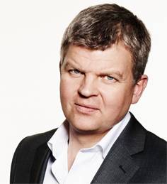 Head and shoulders of Adrian Chiles in black jacket and white open necked shirt