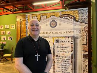 Man dressed in black with cross necklace standing in front of a sign for The Anglican Centre in Rome
