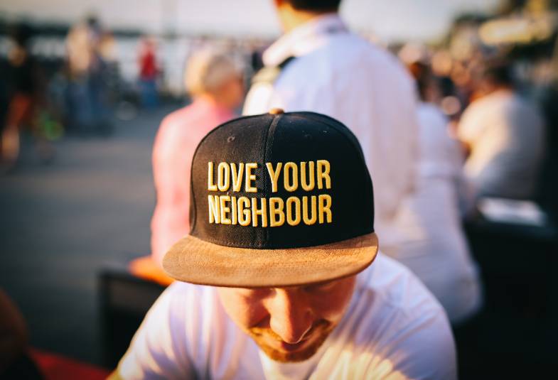 Head and shoulders of a man wearing a baseball hat with the words Love your neighbour on it