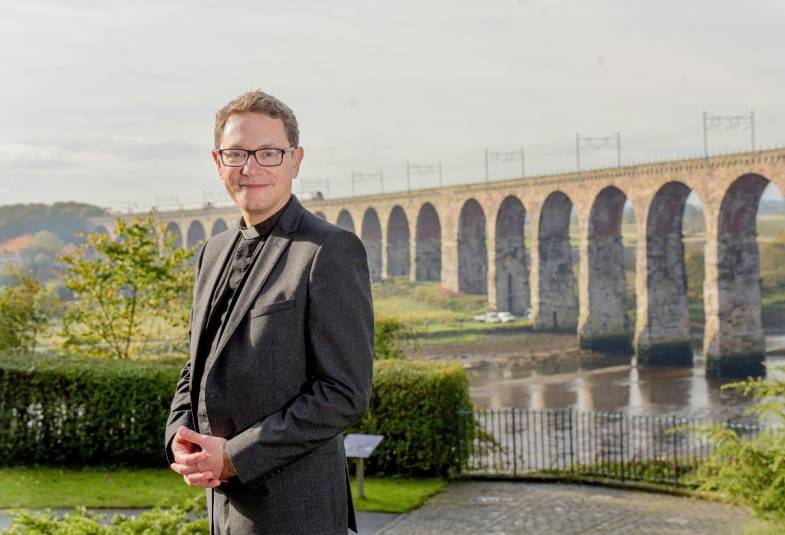 Clergyman standing outside in front of a viaduct