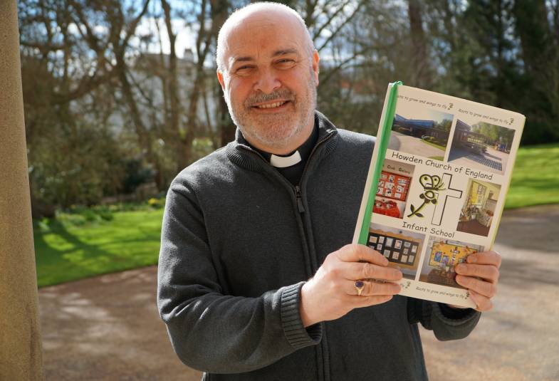 Archbishop standing outside holding an A4 sized book with 5 pictures on the front