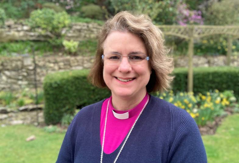 Head and shoulders of smiling woman in clerical clothes, pink blouse, blue jumper