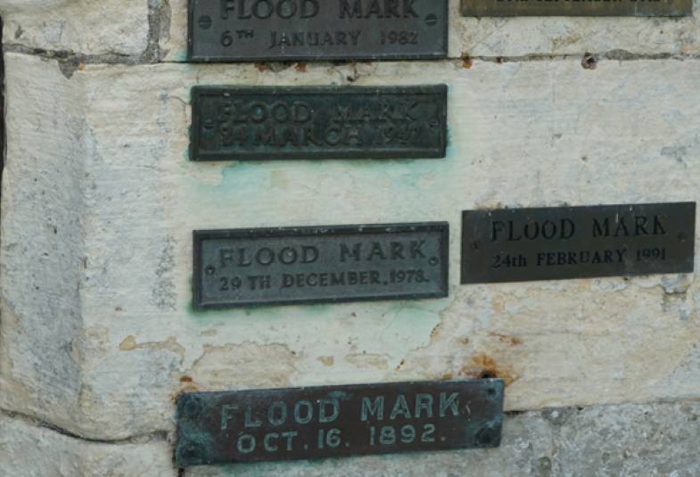 Stone wall with 5 brass plaques on with different dates showing where flood water rose to