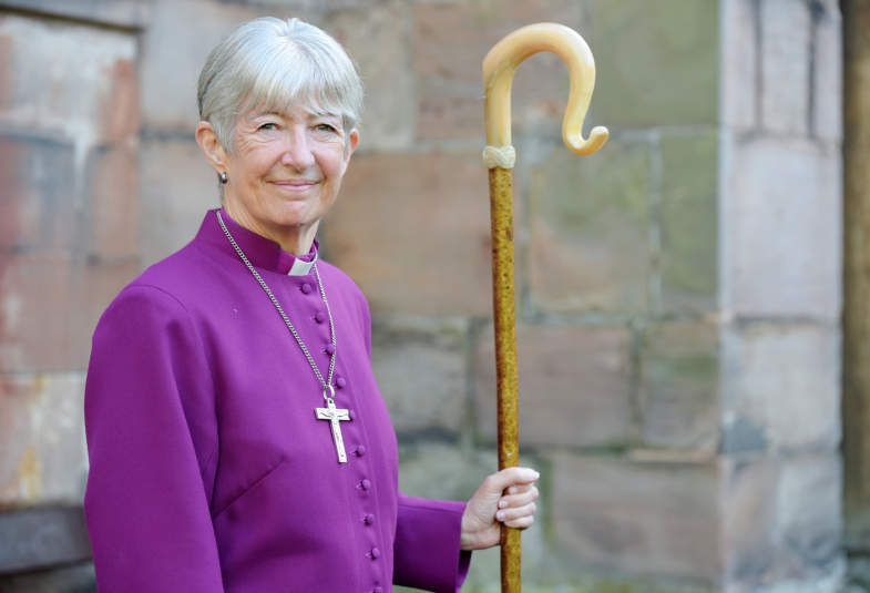 Smiling woman dressed in purple cassock holding a shepherd's crook 