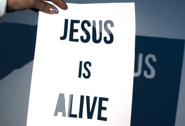 Someone holding a piece o paper with the words Jesus is Alive cut out