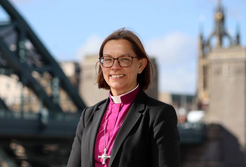 Smiling woman in purple clerical shirt with clerical collar and black jacket