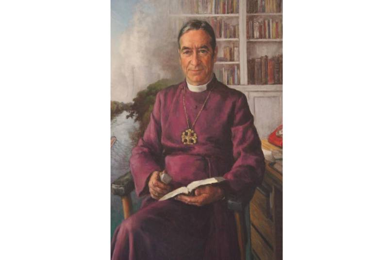 Man in purple cassock seated with books behind him on one side, and a river and landscape on the other