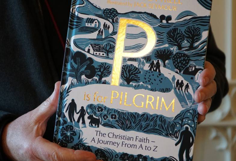 Front cover of a book P is for Pilgrim  in gold lettering on a drawn picture of people following a winding path