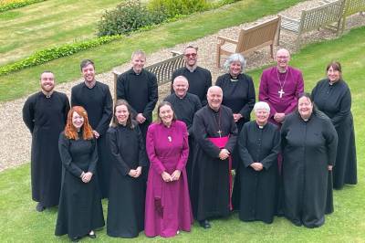 14 people standing outside in a group, dressed in cassocks