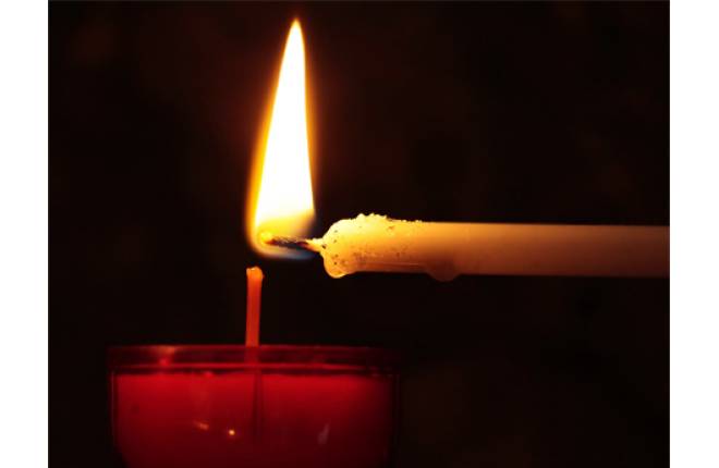 A red candle being lit from a thin white candle - dark background