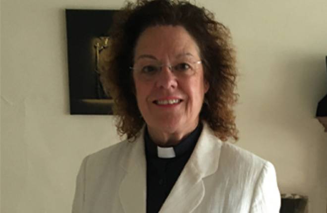 Head and shoulders of female clergy person dressed in black shirt with white jacket