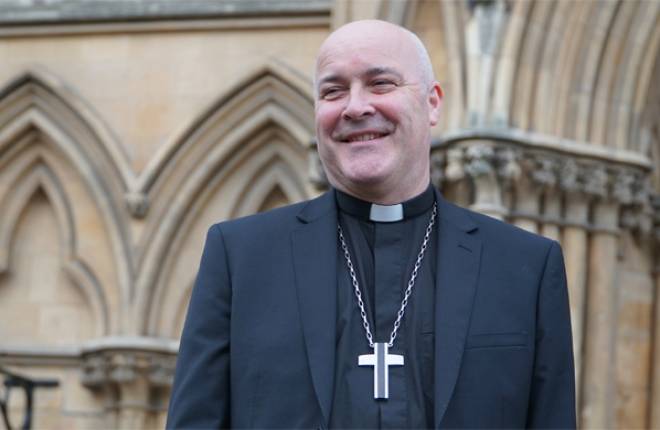 Head and shoulders of Archbishop dressed in black with York Minster behind him