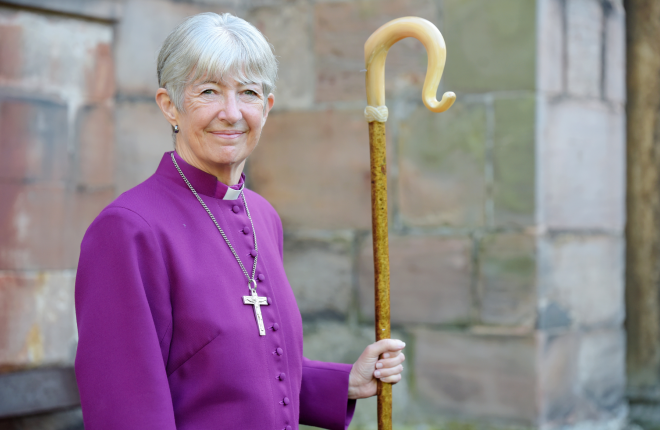 Smiling woman dressed in purple cassock holding a shepherd's crook 
