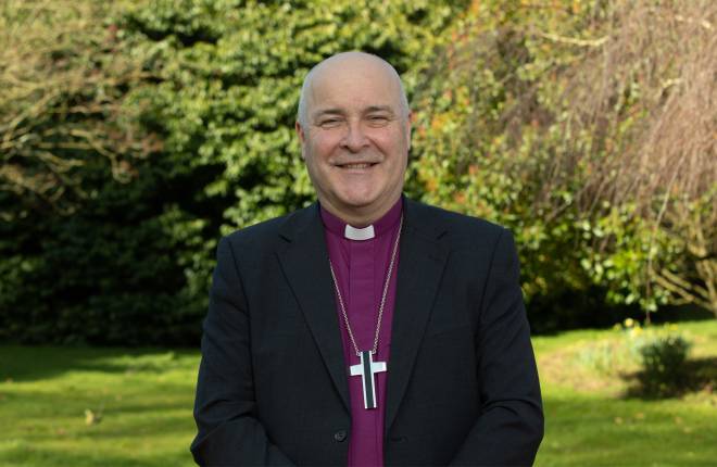 Head and shoulders of the Archbishop standing outside with green trees behind him