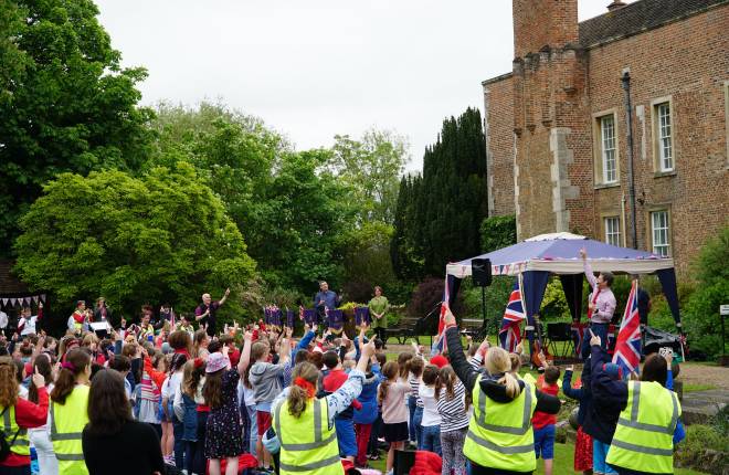 Staff and pupils waving flags together in grounds of large building