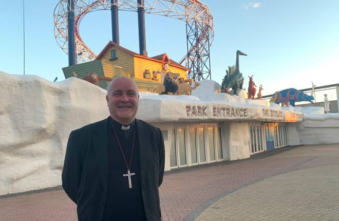 Man in black clerical clothes standing outside an entrance to a amusement park