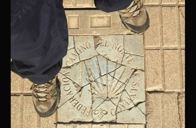 Feet with walking boots standing on a way marker for Camino path