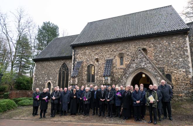 Around 40 men and women dressed in clerical clothes standing outside an old flint stone church